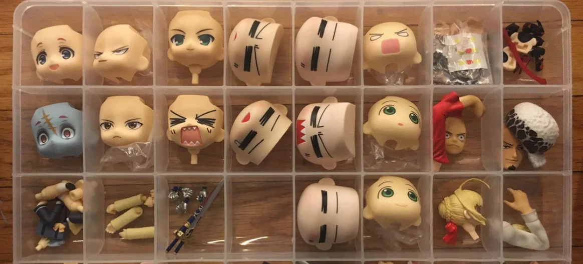 Nendoroid faceplates and spare anime figure accessories stored in a clear plastic compartment organizer box