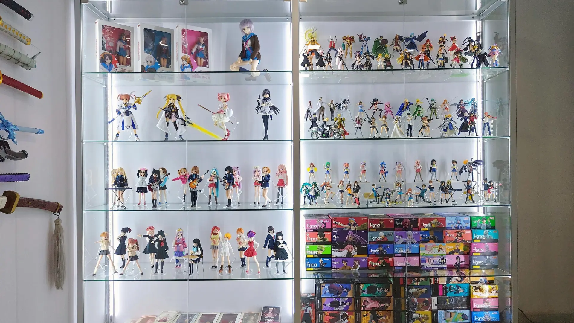 organized anime figure shelf blog A large glass display cabinet illuminated with LED lights, showcasing an organized collection of anime action figures and stacked figure boxes.